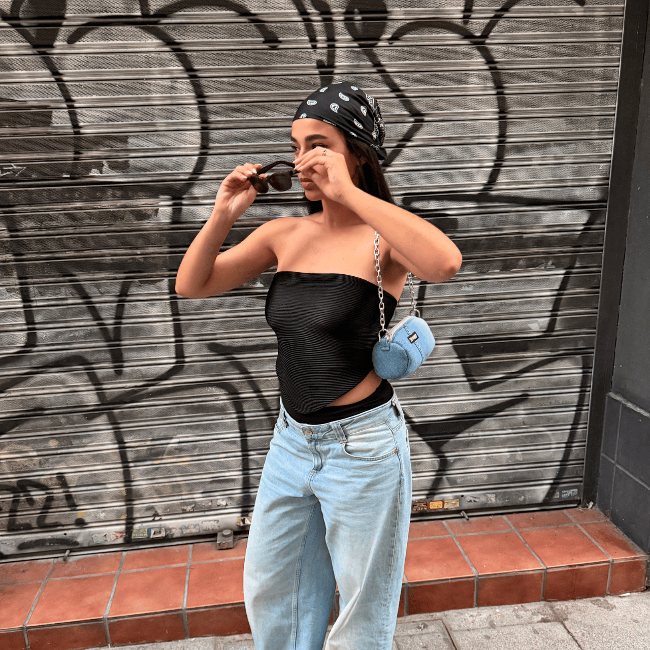 Modelo con la UP2U Jeans Mini Bag de denim reciclado cruzada – look street style con graffiti de fondo